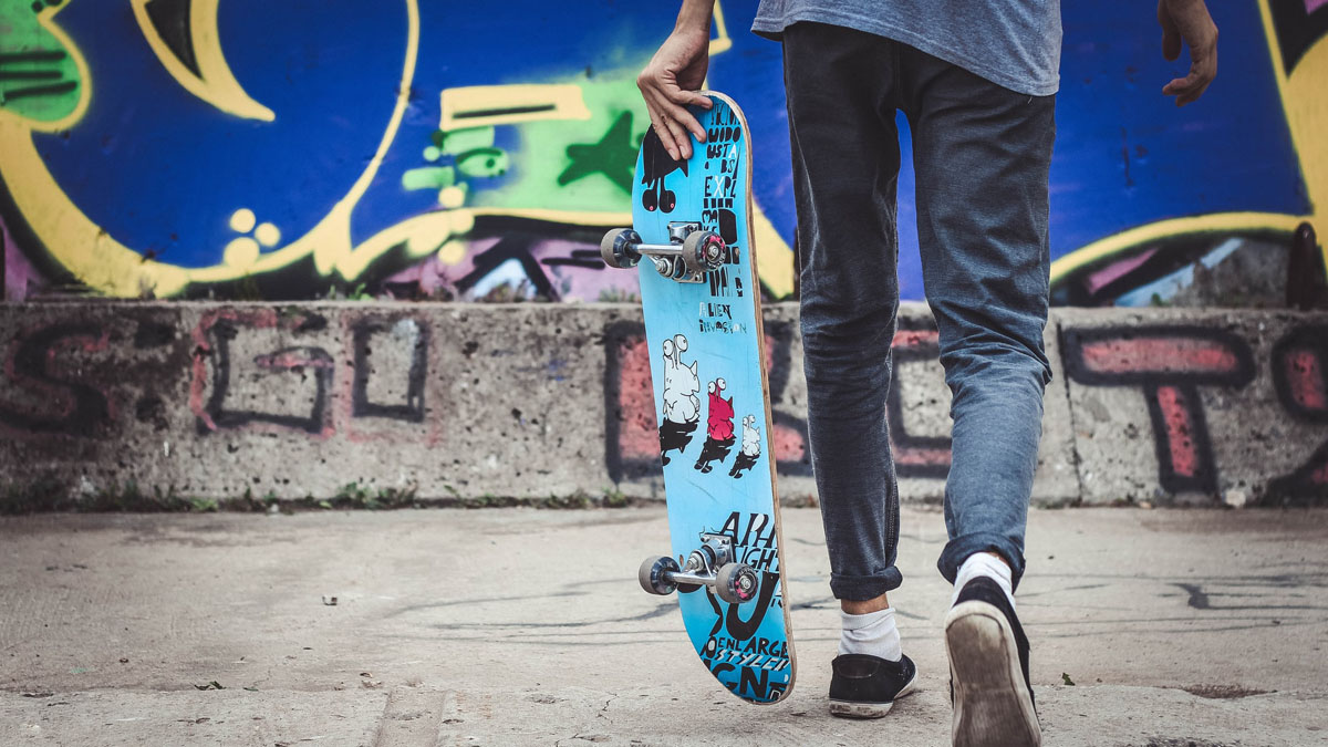 Junge mit Skateboard in der Hand geht auf graffiti-besprühte Wand zu